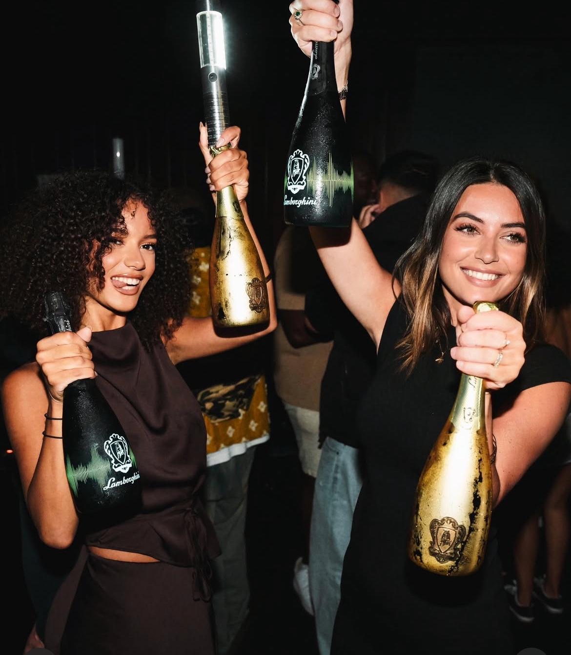 LED bottle service light baton mounted on a Lamborghini champagne bottle, held by a smiling woman bottle waitress in a nightclub celebration