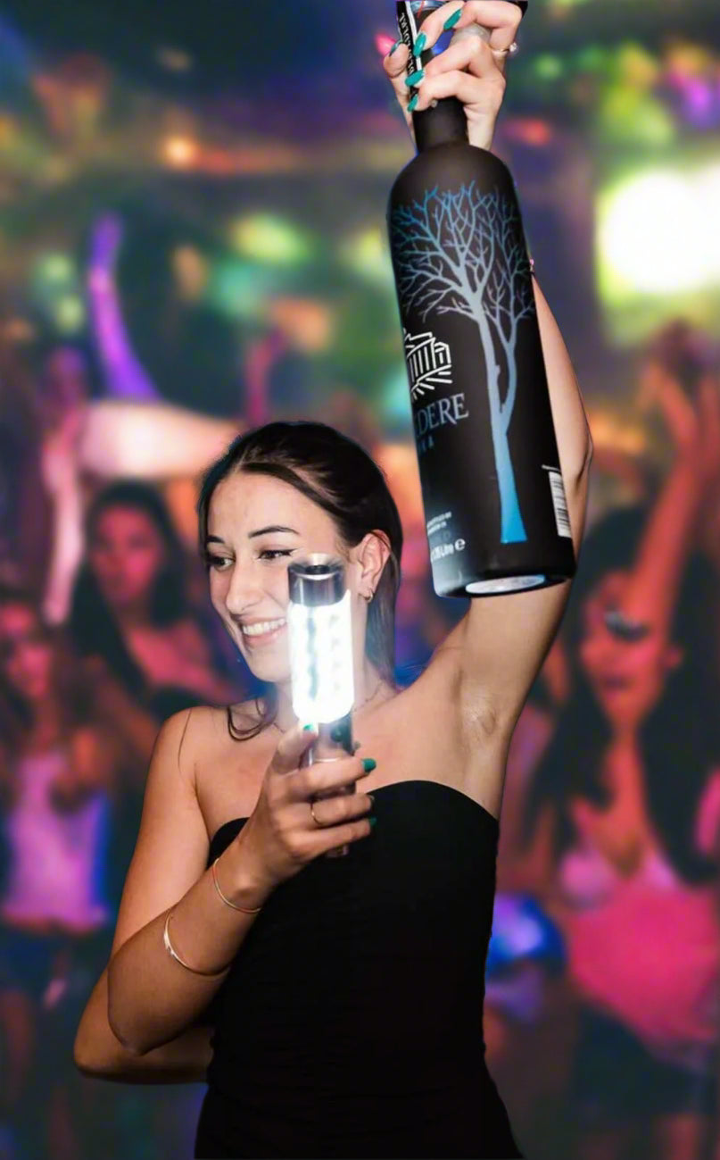 LED bottle service light clipped onto a Belvedere vodka bottle, held by a smiling waitress for bottle service in a nightclub