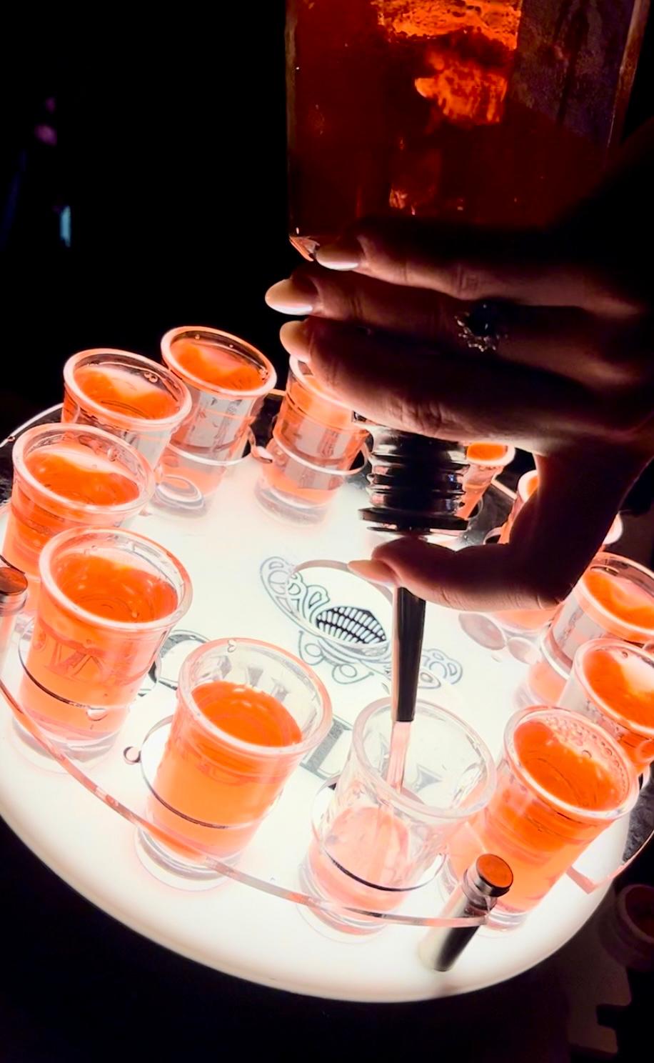 Professional stainless steel speed pourer in use during shot service with LED tray at nightclub